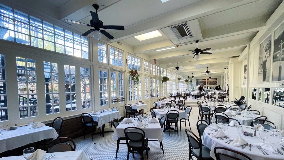 brightly lit white interior of a dining room with tables and chairs at The Court of Two Sisters